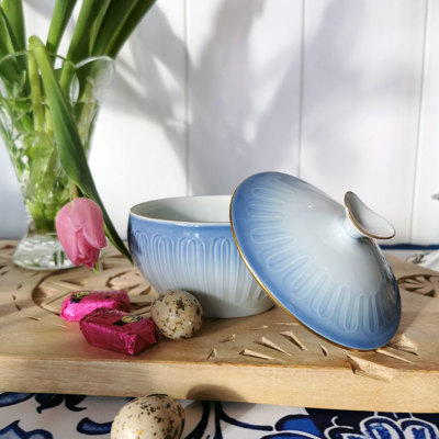 Bing & Groendahl Ballerina sugar bowl in blue and white tones with gold rim. Displayed on a wooden tray with a tulip, chocolate, and Easter eggs.