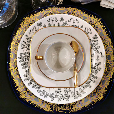 Black, white, and gold table arrangement with a Hackefors King’s cup placed on a Gustavsberg Emigrant plate, and at the bottom a Bjørn Wiinblad Christmas plate used as a charger.