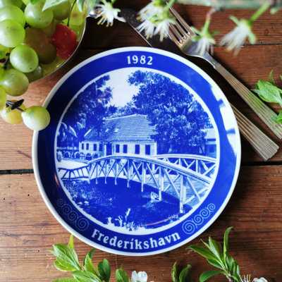 Millhouse porcelænsplatte fra 1982 med motiv af Frederikshavn, præsenteret på et sommerbord med friske druer og grønne grene.