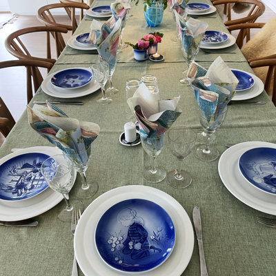 Festive table set for a confirmation or birthday with Désirée Mother’s Day plates, white dinner plates, and wine glasses. Inspiration for party table settings with a green tablecloth and flowers.