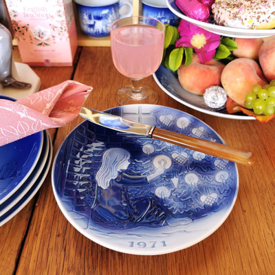 Désirée Christmas plate from 1971 with a Hans Christian Andersen motif used on a spring table. The table is set with a pink napkin, fruit, and cake, creating a cozy atmosphere.