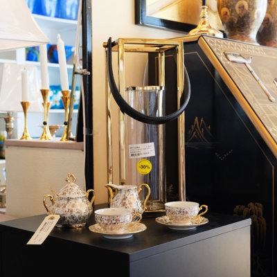 Gilded teapot and cups placed on a black podium next to a modern hurricane lantern and an oriental writing desk – display at the Danish Porcelain House in Odense, Denmark.