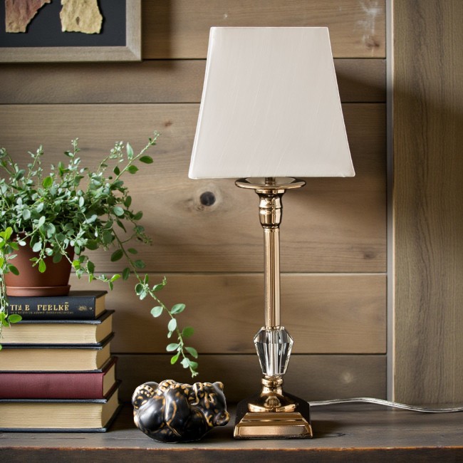 Classic table lamp with golden finish, large crystal detail, and square lampshade placed on side table in cozy interior.