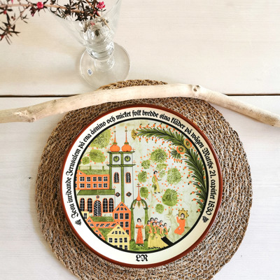 Höganäs plate used as a dinner plate in a rustic table setting with a woven placemat, glass vase, and natural branch as decoration.