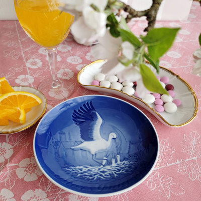 Bing & Groendahl Mother’s Day plate with a stork motif used in a Mother’s Day table setting. On a pink tablecloth with flowers, Offenbach dinnerware, fresh oranges, and pastel-colored chocolate buttons.