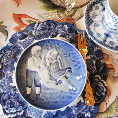 Barnets Dag platte fra 1986 brugt som kagetallerken i en opdækning med blåt mønstret stel, guldbelagt kagegaffel og glas.