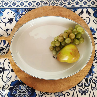 Blue Line dish with a simple blue stripe along the edge, presented on a round wooden board with green grapes and a pear.