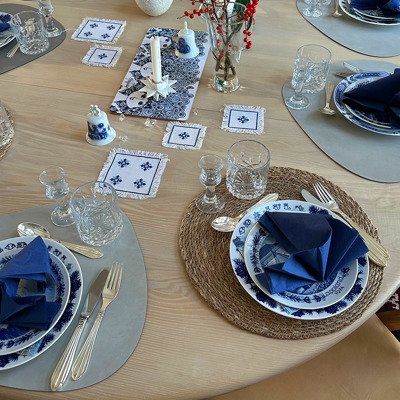 Christmas lunch table setting with a Jenny Nyström Christmas plate for the main course and a Seltmann Swedish landscape plate for the starter. The arrangement in blue and white tones is completed with a napkin and crystal glasses.