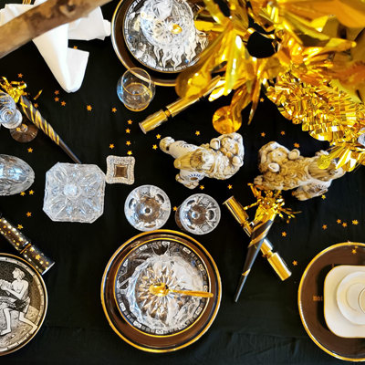 New Year’s table set in black, white, and gold with Rörstrand plates from the Ten Commandments series and Orrefors annual glass plates. Beautiful drinking glasses, festive decorations, and gold details complete the setting.
