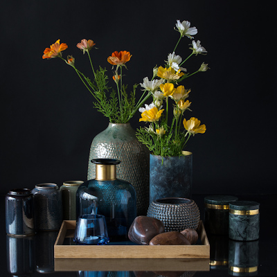 Large vase with blue bottle and small plant pot on tray with vases and marble pots around
