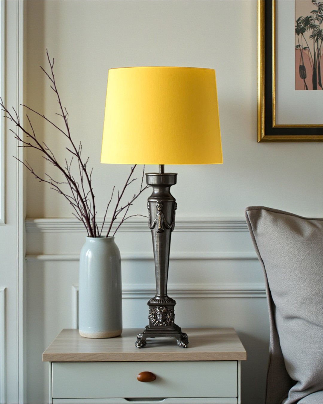 Classic table lamp in patinated bronze with decorative details and yellow lampshade placed by bed in cozy interior.