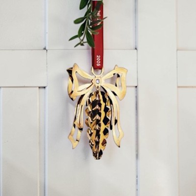 Georg Jensen Christmas mobile 2005 Pine cone in gold finish hanging on a red ribbon on a white wall with a small green branch above.