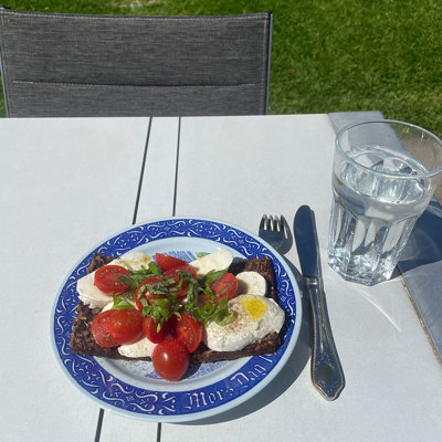 Rörstrand Mother’s Day plate used as a lunch plate with rye bread, mozzarella, and tomatoes. Served outdoors in the garden with a glass of water.